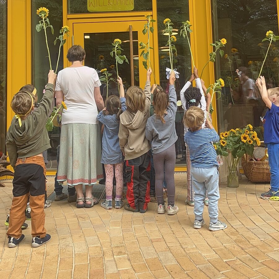 Kinder halten Sonnenblumen vor dem Eingang des Kindergartens hoch