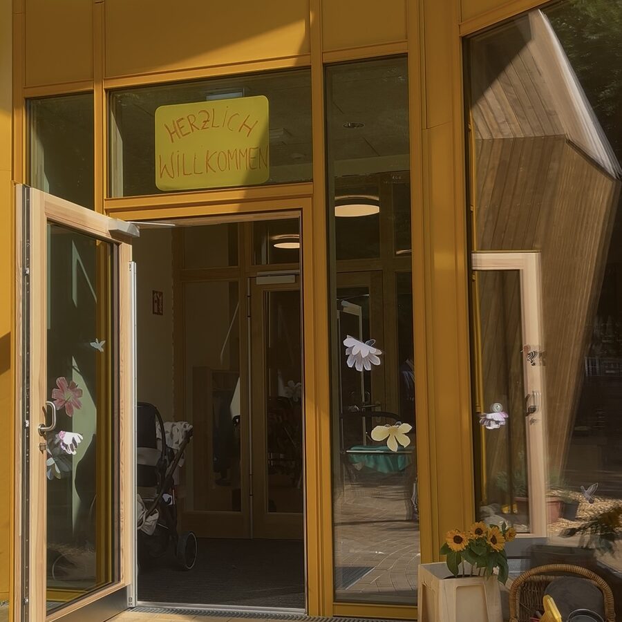 Geöffnete Eingangstür des Kindergartens mit einem Schild Herzlich willkommen